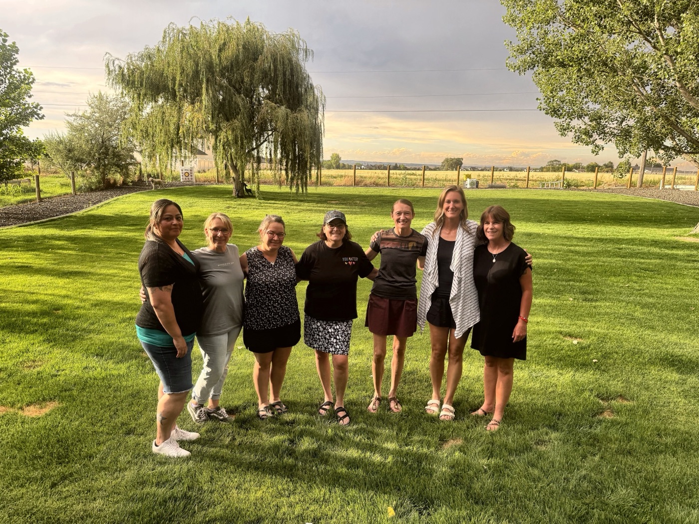 A group of Ugly Cry Club moms standing together on a lawn at sunset